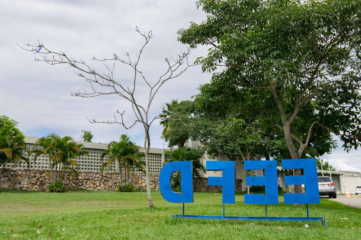 Fotografia, em dia nublado, da Escola de Educação Física e Desportos. Na parte inferior da imagem, está o letreiro EEFD, na cor azul, fixado no gramado.